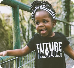 Close up of child smiling on bridge with shirt with text that says Future Leader