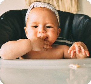 Infant in high chair reaching for a cracker